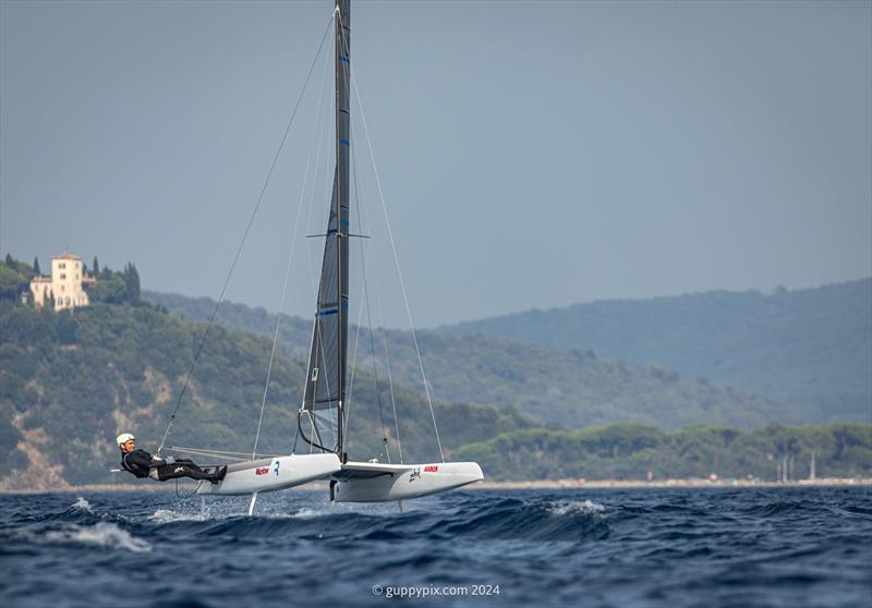 A Class Cat Regata Nazionale - The 2022 World Champ Ravi Parent USA 76 races with the iconic Punta Ala ‘White House' overlooking the Golfo Di Follonica photo copyright Gordon Upton / www.guppypix.com taken at Centro Velico Punta Ala and featuring the A Class Catamaran class