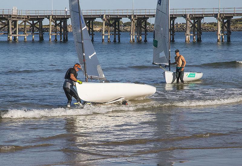 The legend that is Anthony 'Nocka' Nossiter with his Finn on the dolly as Olympian Jake Lilley also comes ashore after training - photo © John Curnow