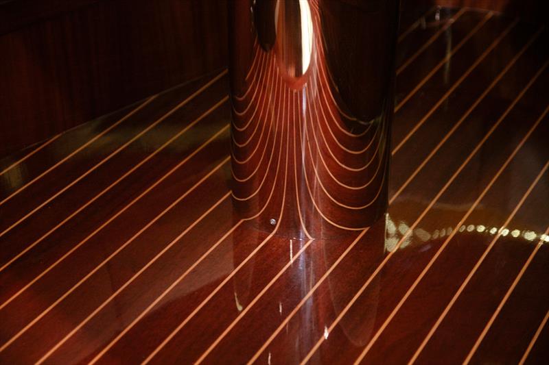 Hand-laid mahogany underfoot, its caulk lines mirrored in the polished steel table foot - photo © J Craft Boats